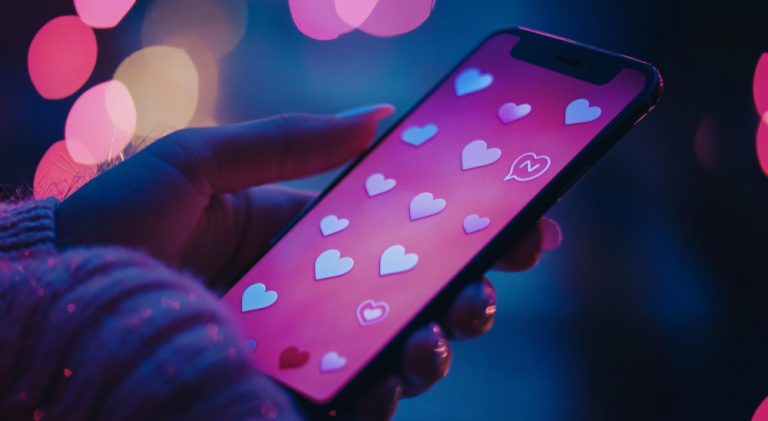Um mockup de celular com corações rosas como fundo de tela. A imagem representa apps de bate-papo para a sua idade.