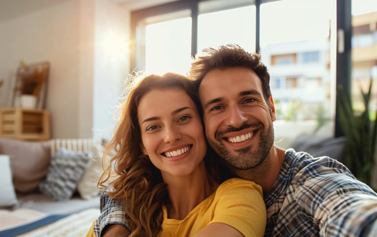 Um selfie de casal sorrindo em uma sala de estar. A imagem representa apps e sites de bate-papo.